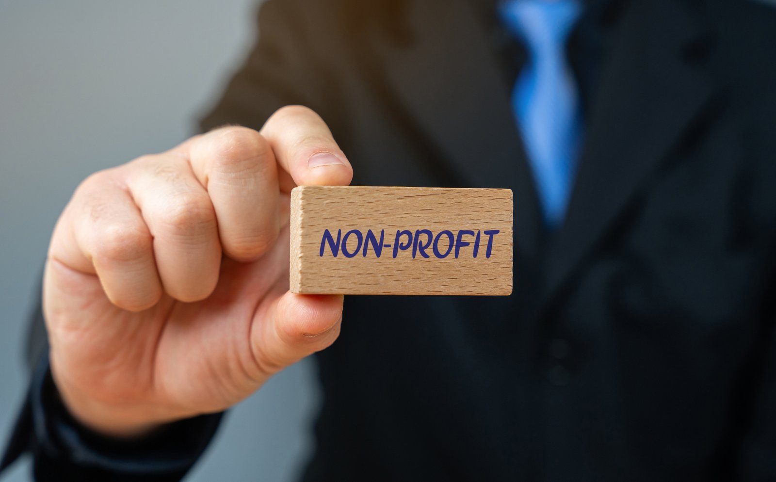 block with the word non profit. organization that operates for a purpose other than generating profit for its owners or shareholders. businessman holding wooden block in his hands